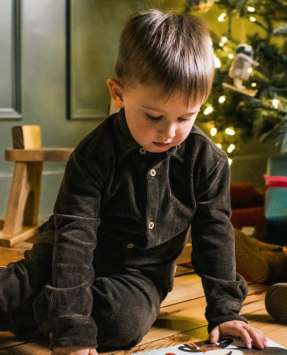 Toddler boy wearing a dark outfit beside a Christmas tree