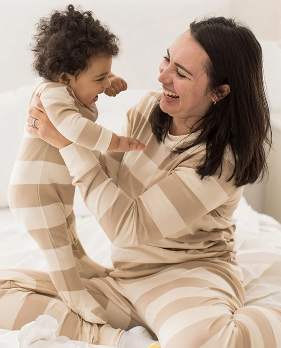 Parent holding a child in matching neutral striped pajamas